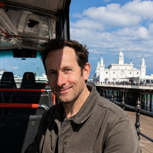 Oliver Bennett, Brighton bus tour guide and local sightseeing specialist, on the open-top bus with Brighton Palace Pier behind